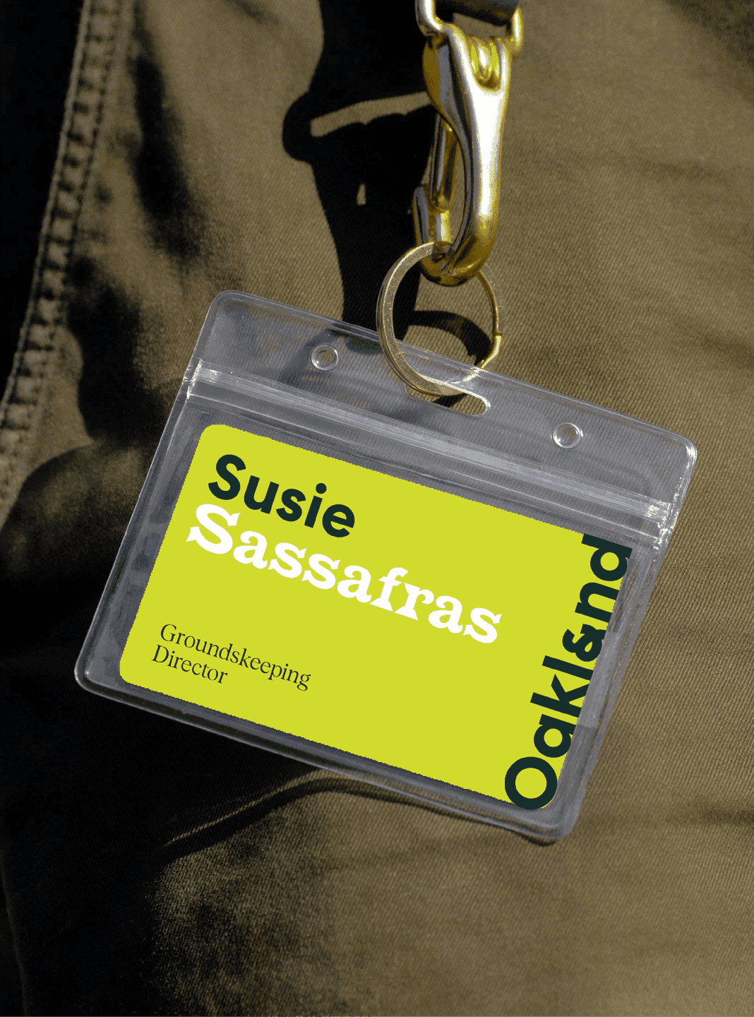 A bright Oakland-branded staff badge with bold typography hangs from a lanyard, featuring the name Susie Sassafras.